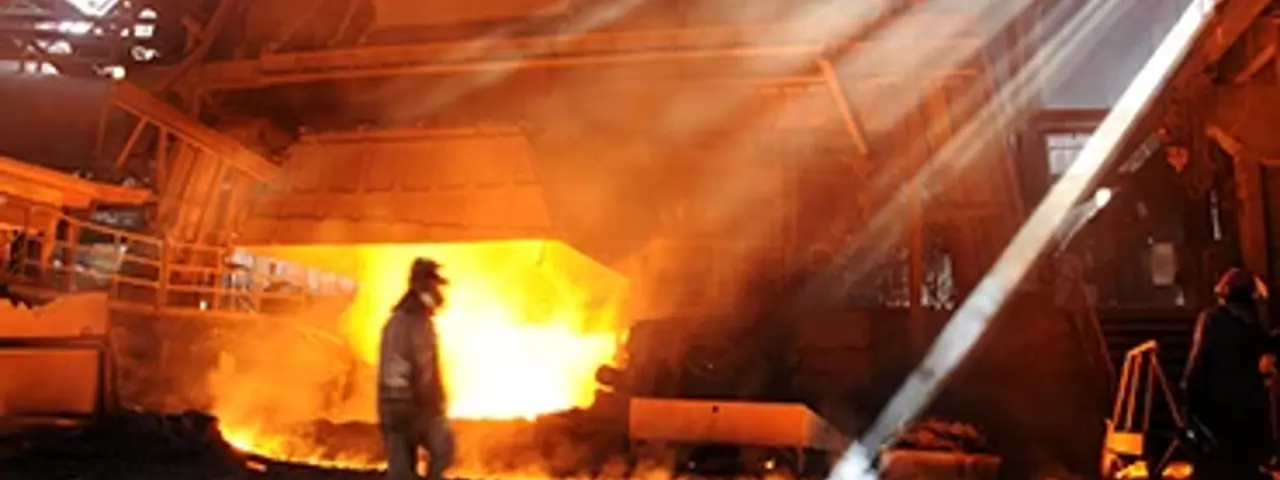 A molten metals worker walking across a factory infront of an open furnace door